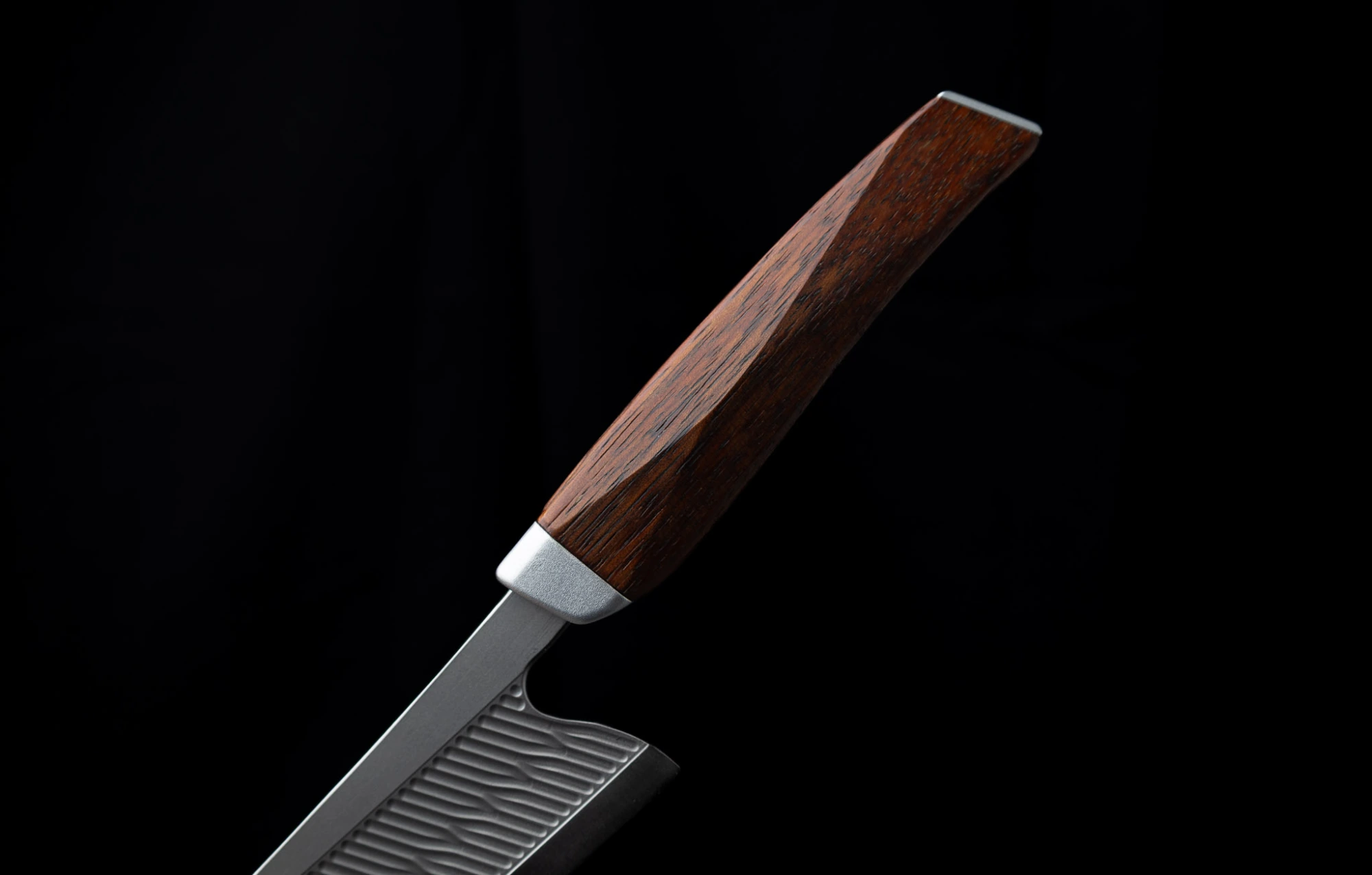 Nahaufnahme eines RYVON Knives Küchenmessers mit einem dunklen Holzgriff und einer strukturierten Metallklinge auf schwarzem Hintergrund.