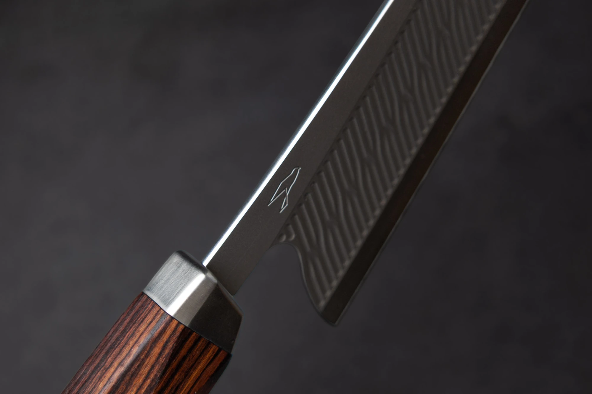 Nahaufnahme eines RYVON Knives Küchenmessers mit strukturierter Klinge und einem Holzgriff vor grauem Hintergrund.